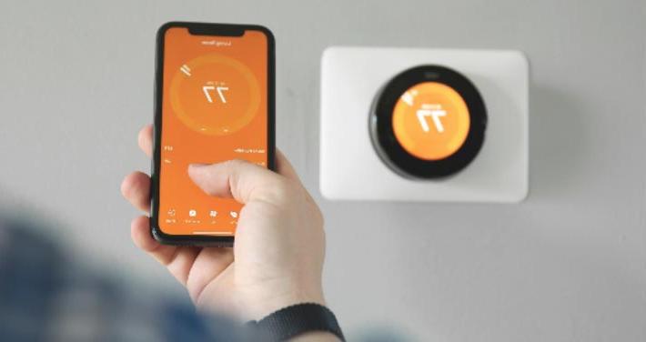 person holding smart phone in front of smart thermostat